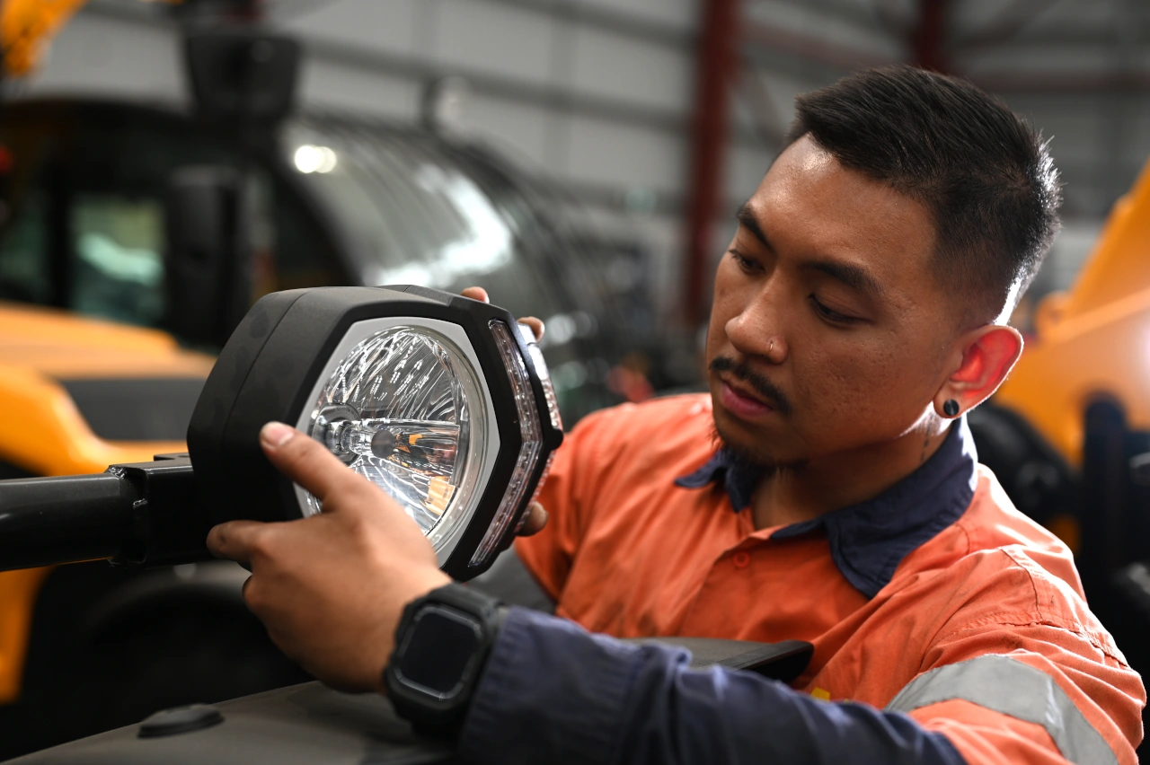 A mechanic inspecting a headlight on a dieci telehandler