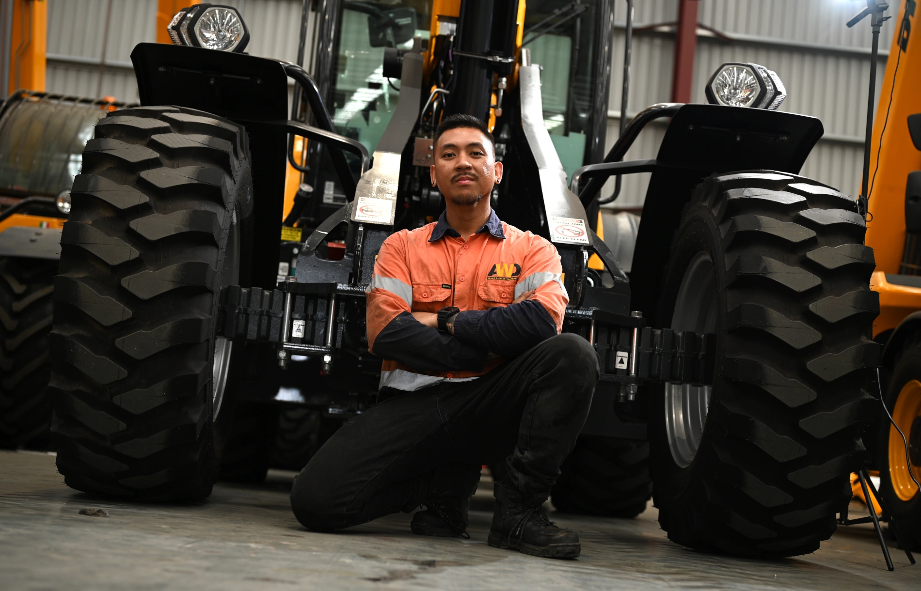 an AWD service technition crouching in-front of a Dieci telehandler discussing the machines steering modes - 2WS, 4WS and crab steer