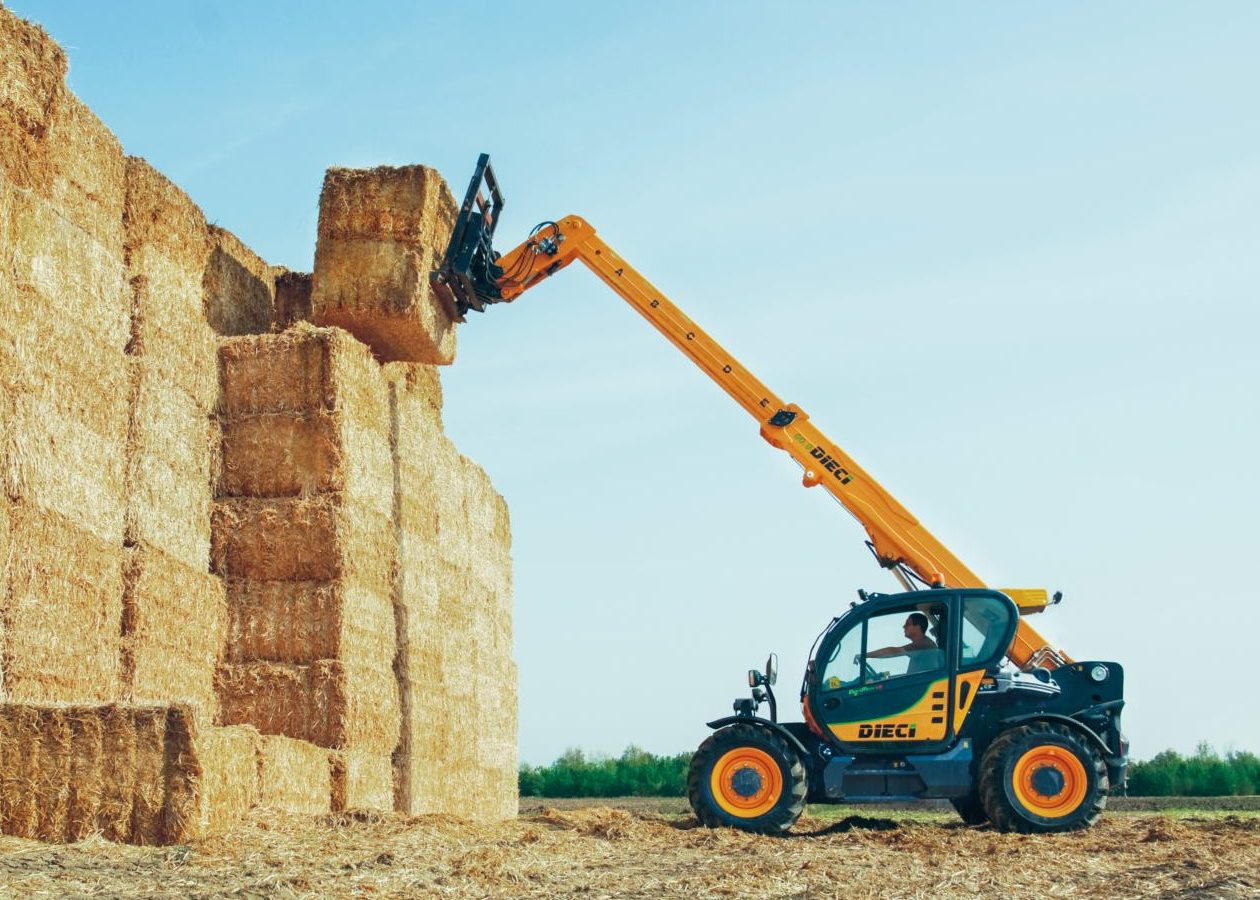 A Dieci telehandler lifts a hay bale towards stacked bales