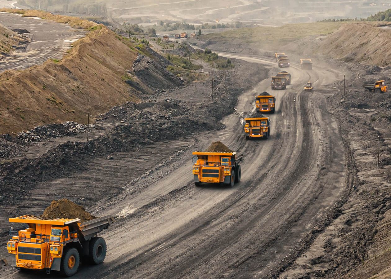 Dieci Dump trucks transport material along a curved, dusty road in a mining site landscape.