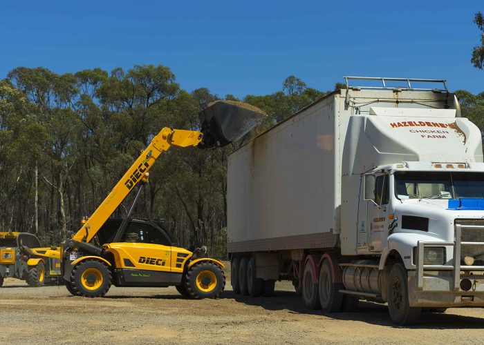right side view of a Poultry Pro 3t Telehandler tipping poultry materials into a large truck