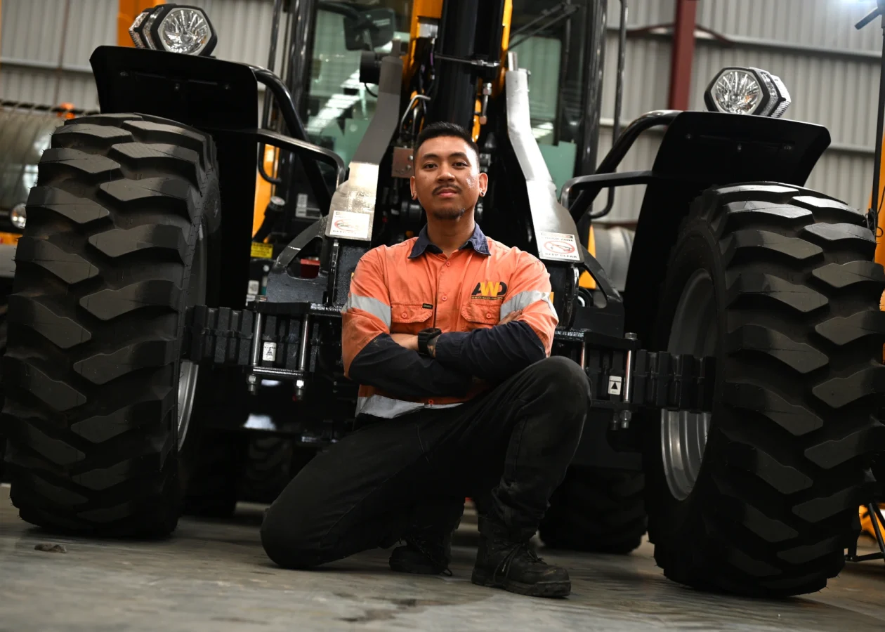 an AWD service technition crouching in-front of a Dieci telehandler discussing the machines steering modes - 2WS, 4WS and crab steer